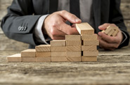 A man in a suit layers wooden building blocks