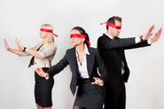3 business people blindfolded and feeling their way around