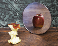 A mirror is placed behind an apple core, showing a full uneaten apple