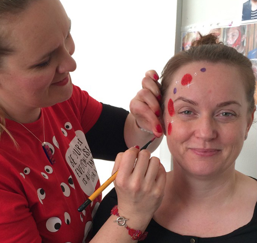 A woman having her face painted with red and purple blobs 