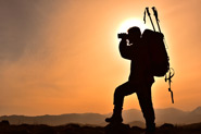 a man with camping equipment looks through binoculars 