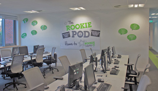 A space filled with desks and computers, with a large poster saying 'The Rookie Pod' on the walls