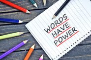 A notepad with the phrase 'Words have power' written in capital letters. Surrounding the notepad are a number of coloured pencils