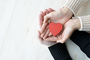 Two people hold their hands palm upwards, with a red heart on the top