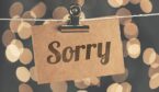 The word sorry is etched onto a piece of wood, clipped to a clothes line