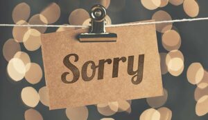 The word sorry is etched onto a piece of wood, clipped to a clothes line