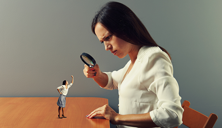 Woman inspecting a smaller version of herself with a magnifying glass