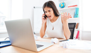 A frustrated woman is on the phone, looking cross at ther laptop