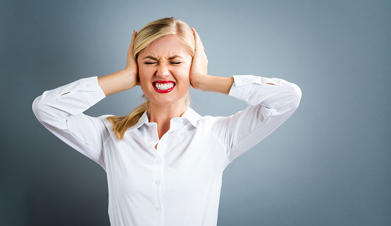 Young woman blocking her ears on a gray background