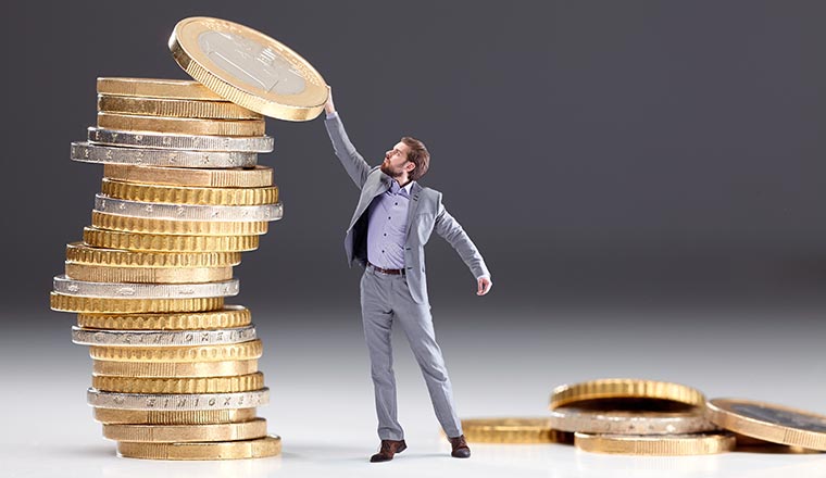 a tiny man puts a euro on top of a stack of euros