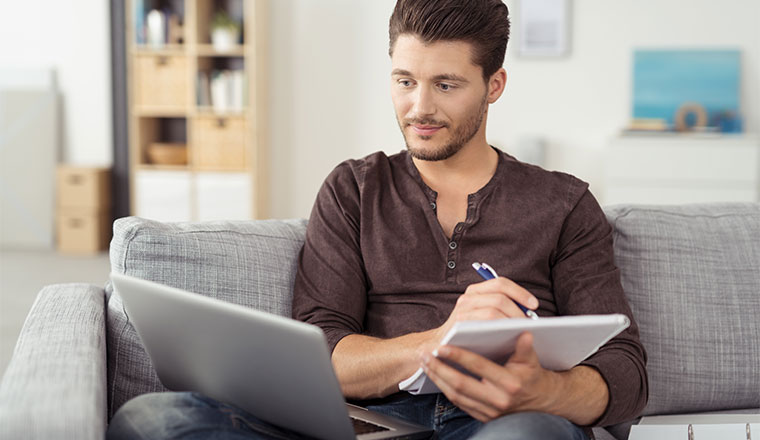 A man takes note whilst looking at his laptop