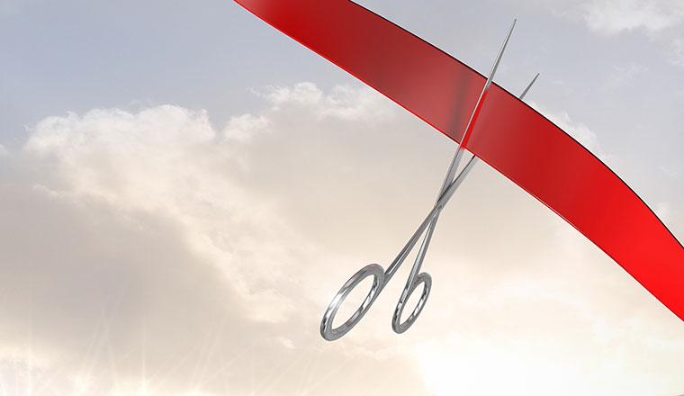 A pair of scissors are cutting a red ribbon
