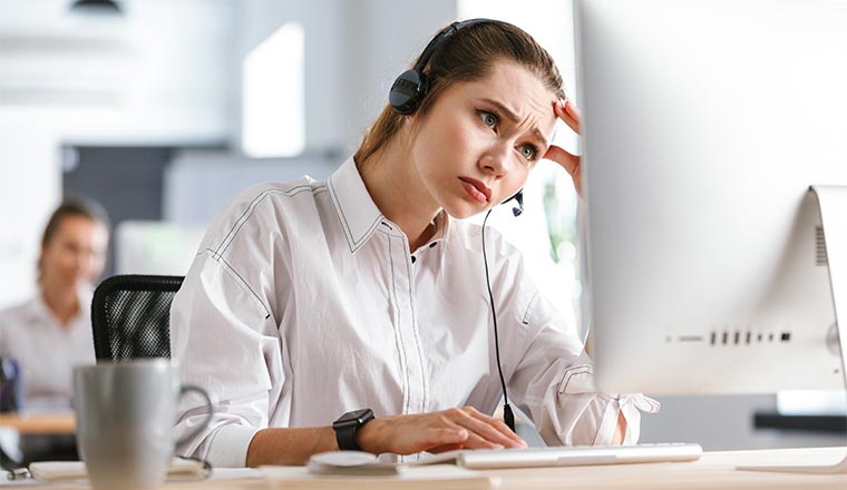 frustrated young woman wearing microphone headset dressed in shirt sitting at her workplace at the office,