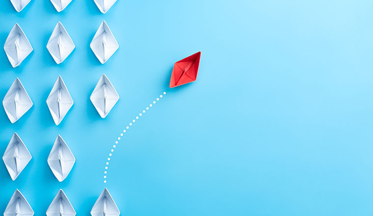 Group of white paper ship in one direction and one red paper ship pointing in different way on blue background. Business for innovative solution concept.