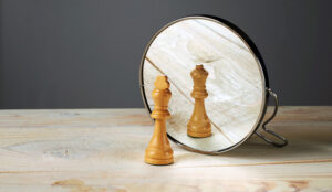 A wooden chess queen piece is reflected by a mirror