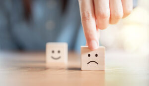 An unhappy face on a building block is held by a hand