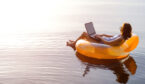 A woman floats on water with an orange inflatable with her laptop