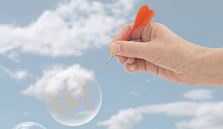 A bubble is burst by a hand holding a dart