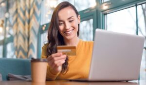 enthusiastic woman reading credit card number while staring down and working on laptop