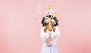 A woman throws confetti into the sky, with a pink background