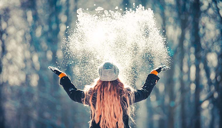 Young woman throwing snow in the air at sunny winter day, back view