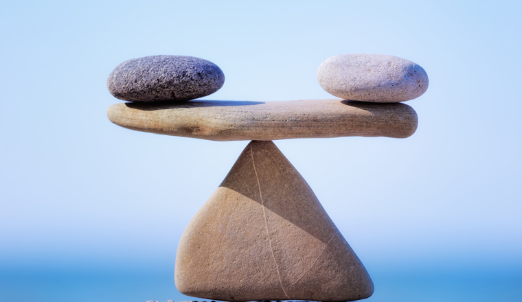 Two zen stones balance on a larger zen stone with a peaceful background