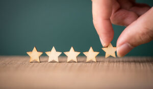 Hand putting wooden five star shape on table. The best excellent business services rating customer experience concept.