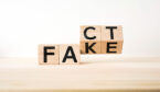 Geometric wooden cube with word " FACT FAKE " on wood floor and white background