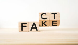 Geometric wooden cube with word " FACT FAKE " on wood floor and white background