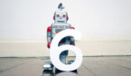 A small robot toy holds the number 6