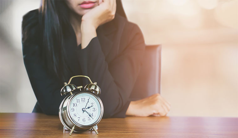 A clock is sat on a desk in front of a bored looking lady