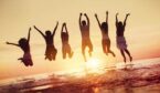 Big group of happy friends having fun and jumps in water against sunset