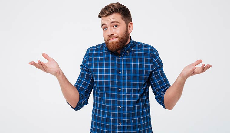 A photo of Confused young bearded man standing and shrugging shoulders