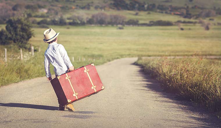 A photo of a child carrying a suitcase down the road