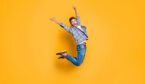 A photo of cheerful man in sneakers, denim outfit, jumping with raised arms