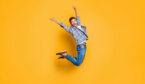 A photo of cheerful man in sneakers, denim outfit, jumping with raised arms