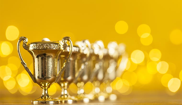 A photo of award trophies against bright yellow background with blurred lights