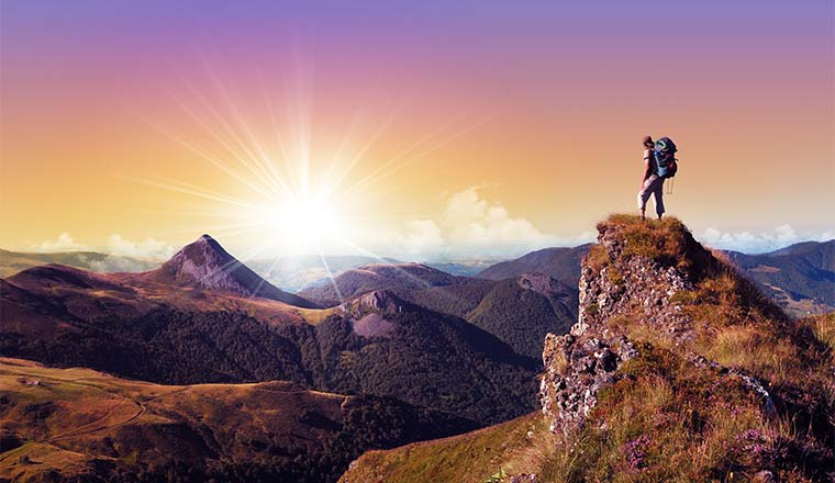 A photo of someone standing on a cliff staring at the sun