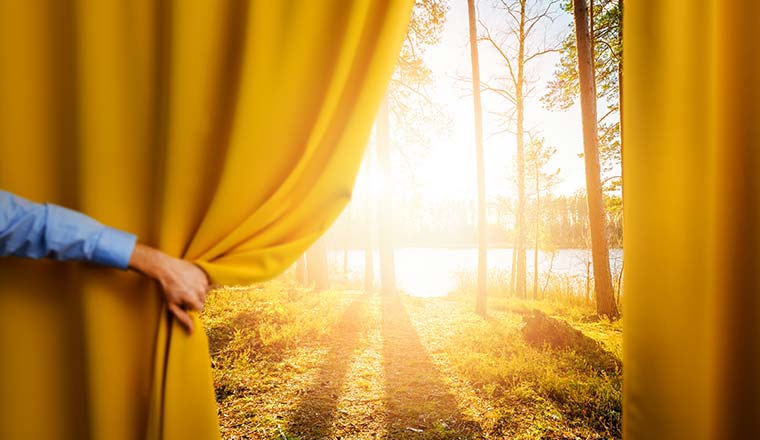 A picture of a hand opening curtains onto a pretty landscape