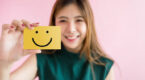 Happy person holds up a post it note with a smiley face on it