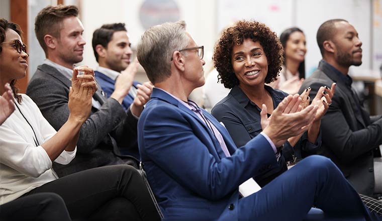 A photo of an audience as they talk and clap