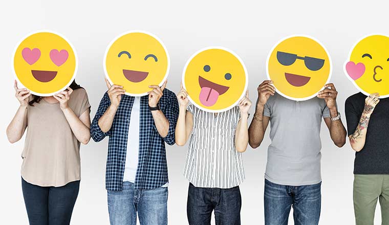 A group of people hold emoticons over their faces