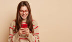 A woman wearing red glasses smiles as she looks at her phone