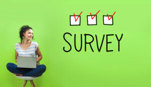 A woman sat on a chair on a laptop,looks at the word survey with boxes ticked