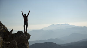 A man stands on a rock with his hands punched in the air