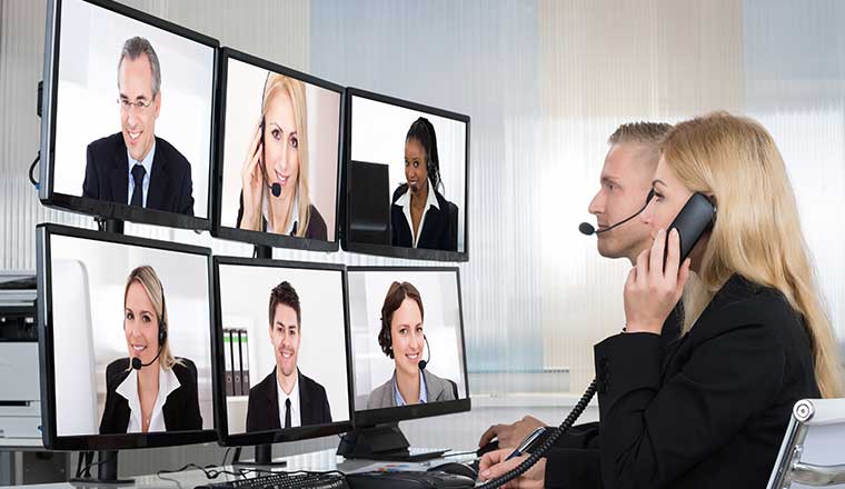 A woman on the phone talks to a group of people on different monitors