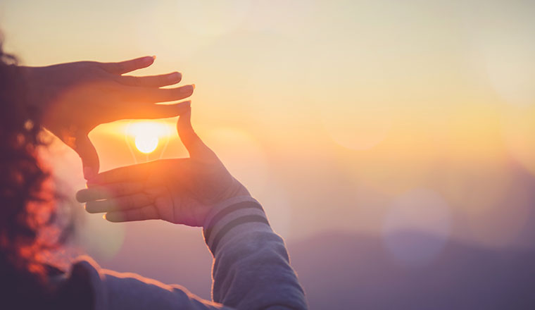 A photo someone using their hands to frame the sun