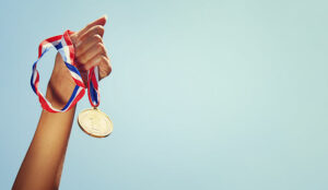 woman hand raised, holding gold medal against sky. award and vic