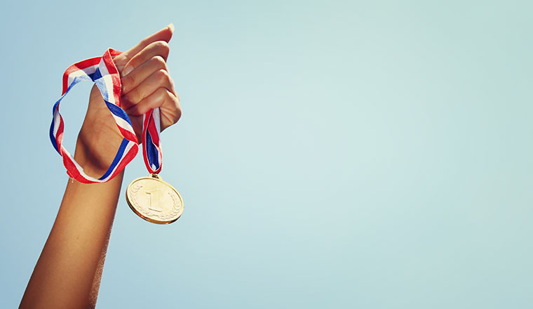 woman hand raised, holding gold medal against sky. award and vic