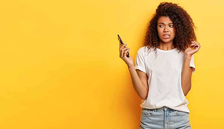 A woman stands in front a yellow wall, she holds the phone away from her in disgust